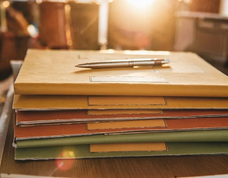 Several stacked folders with a pen resting on top, illuminated by warm sunlight.